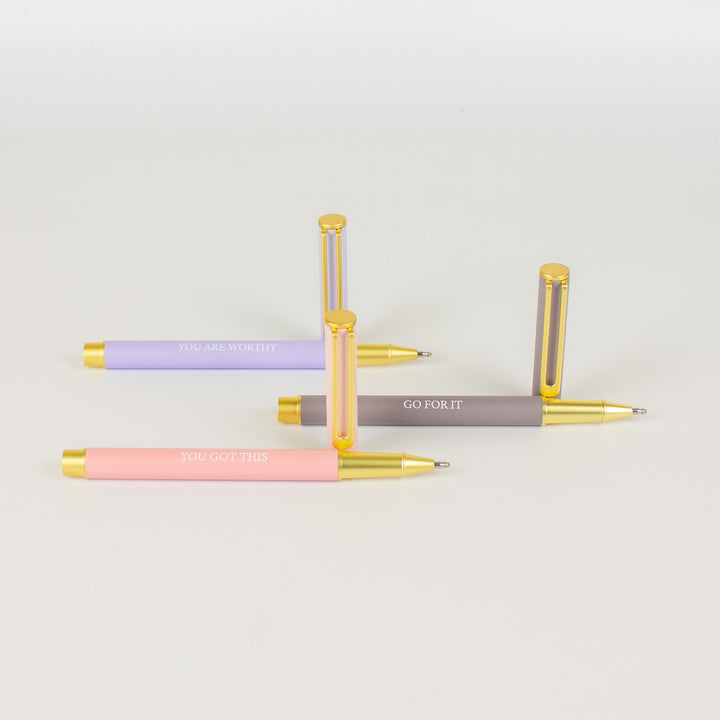 A set of three metal pens in pink, lilac, and gray colors with white lettering, each pen has a cap and is designed with a sleek metallic finish.