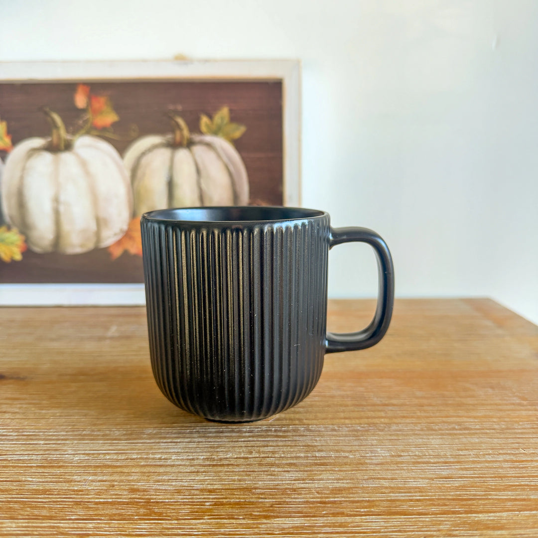 Black mug on a wooden surface with a framed picture of pumpkins in the background