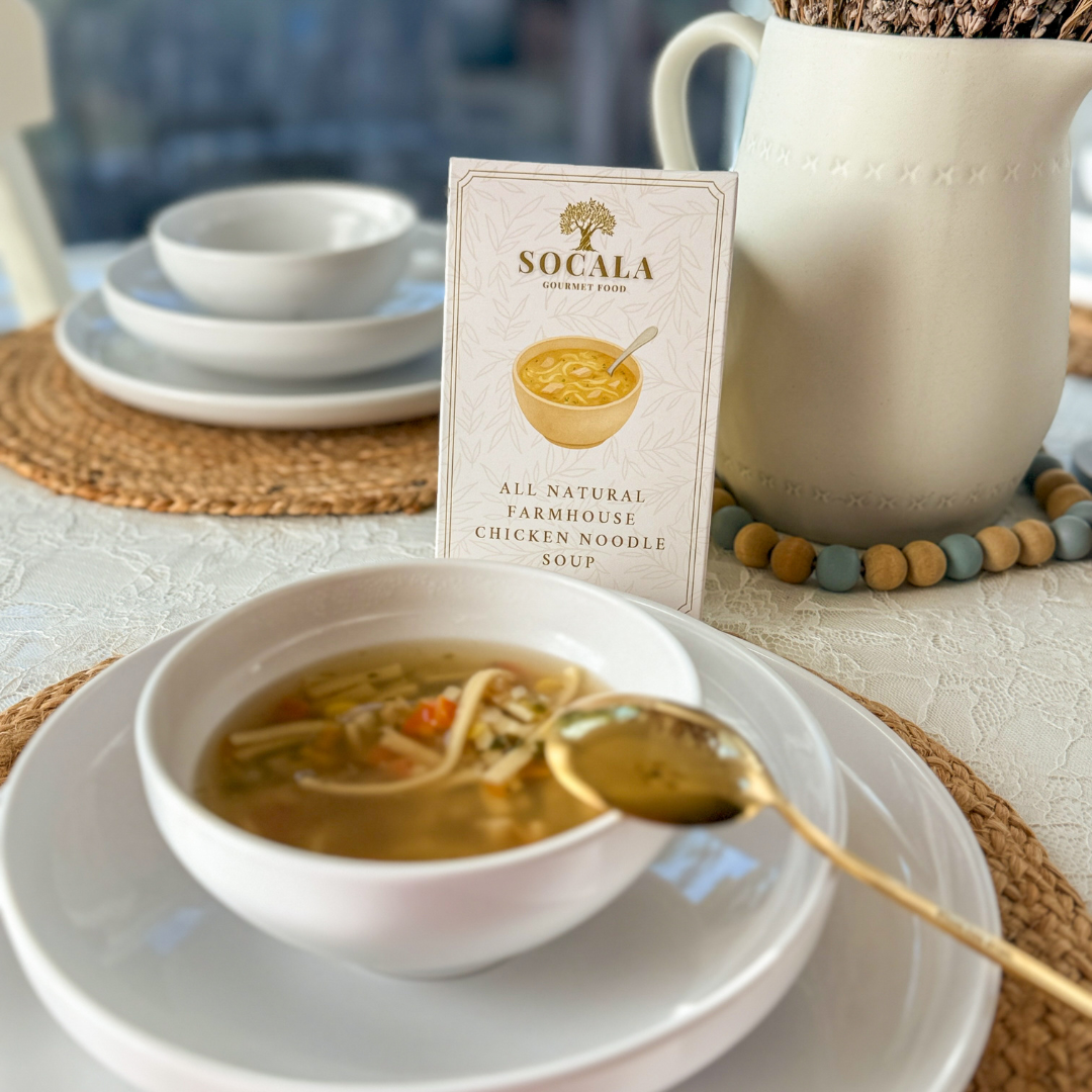 Bowl of soup with a spoon on a plate, featuring a Socala product box.