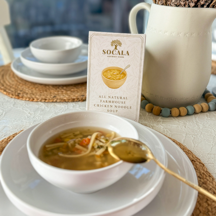 Bowl of soup with a spoon on a plate, featuring a Socala product box.
