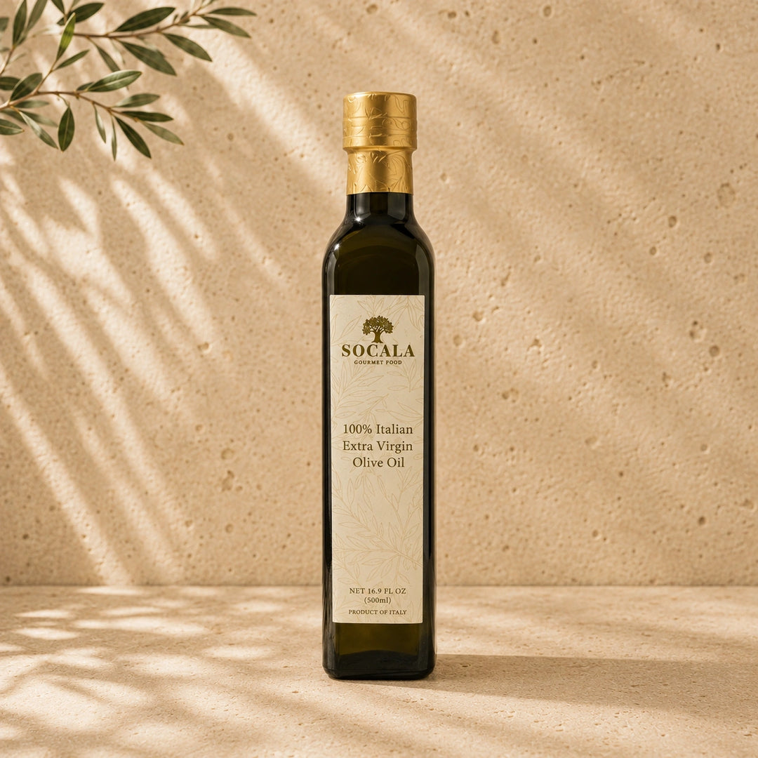 A bottle of Socala 100% Italian Extra Virgin Olive Oil stands on a beige stone-like surface with warm sunlight and leaf shadows cast across it. The bottle is dark glass with a gold cap and a cream label featuring the Socala brand name.