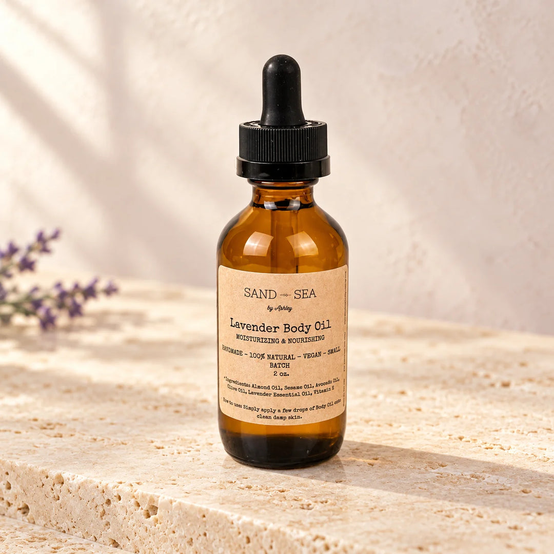 An amber glass dropper bottle of Sand-Sea by Jazzy Lavender Body Oil, set on a textured beige stone surface with soft shadows and a blurred lavender sprig in the background.