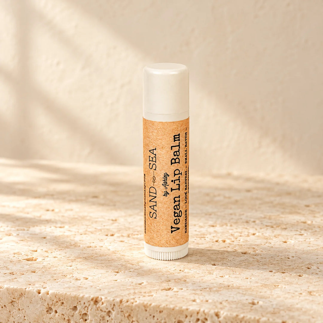 A single tube of Sand of Sea Vegan Lip Balm stands upright on a textured stone surface with warm natural shadows cast across the scene.