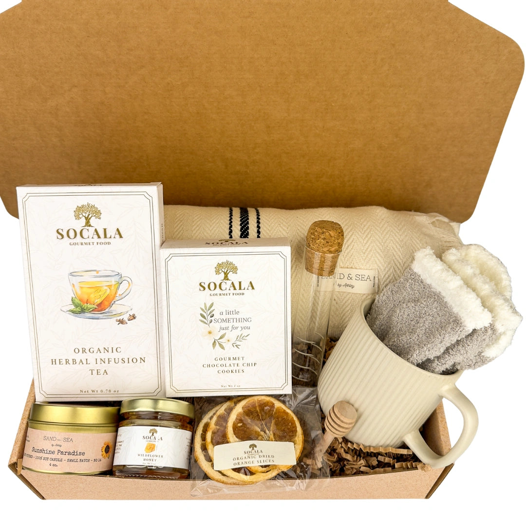 Blanket and tea gift set with SOCALA tea bags, a mug, and various tea-related items in an open cardboard box.