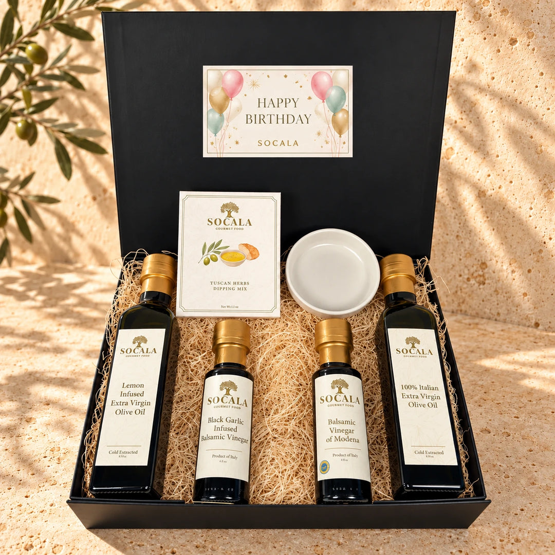 Socala gift set in an open kraft box with a 'Happy Birthday' message, containing four olive oil bottles, a peppercorn roasting box, and a small white bowl filled with red and green shredded paper.