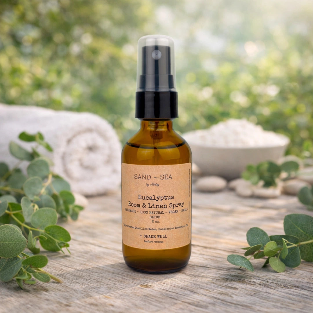 Bottle of Sand & Sea Eucalyptus Room & Linen Spray on a wooden surface with greenery.