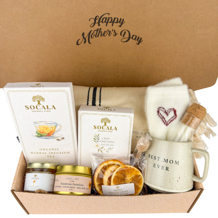 Gift box with 'Happy Mother's Day' on a brown background, containing tea, candles, and a mug.