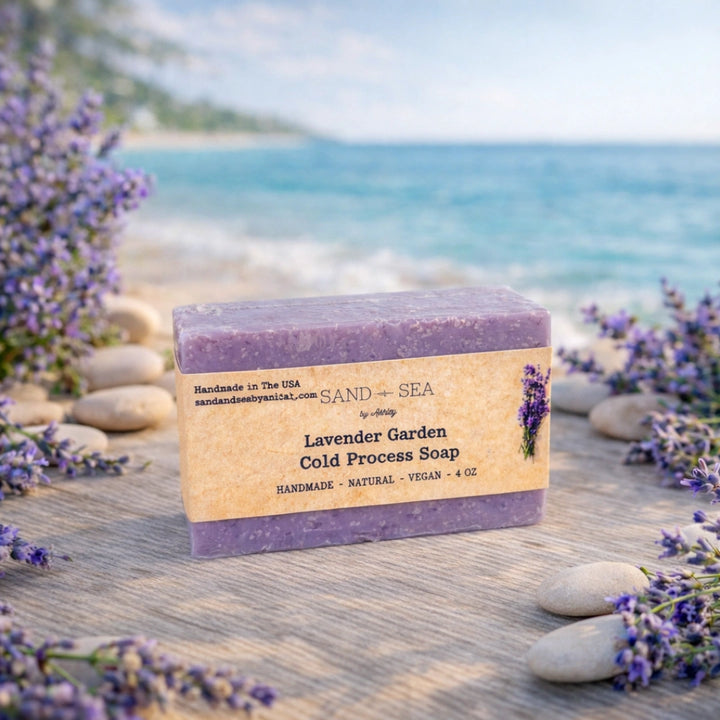 Lavender Garden Cold Process Soap by The Sand and Sea on a wooden surface with lavender flowers and a beach background.