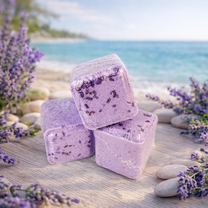 Three purple shower steamers with lavender flowers on a wooden surface near a beach.