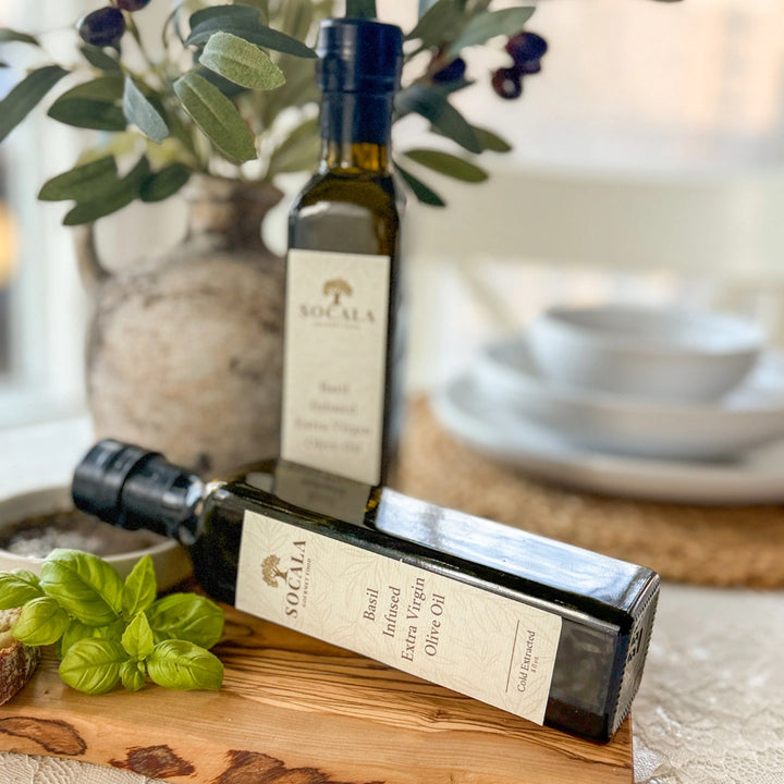 Two bottles of Socala olive oil on a wooden board with a blurred background