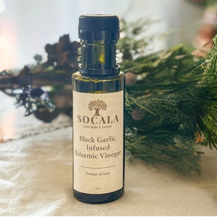 Bottle of Socala Black Garlic Infused Balsamic Vinegar on a textured surface with greenery in the background