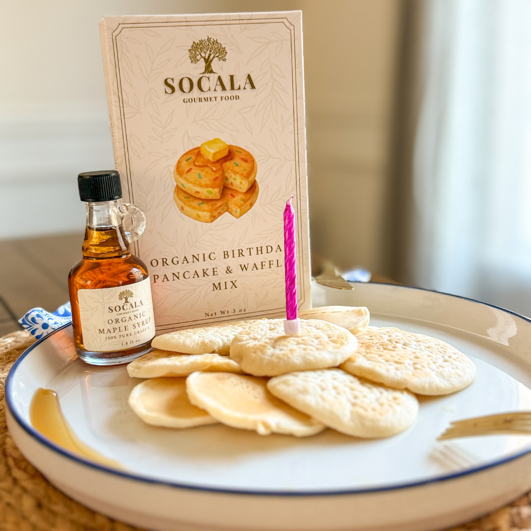 Plate with pancakes, syrup, and a candle next to Socala Gourmet Foods packaging.