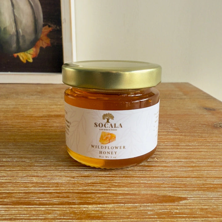 Jar of Socala Wildflower Honey on a wooden surface with a blurred background
