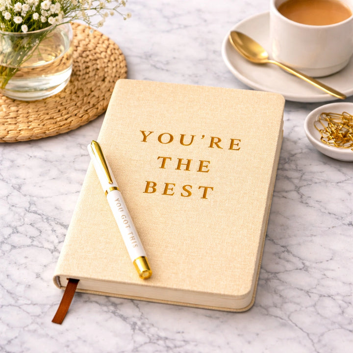 Notebook with 'You're the Best' on a marble surface with a cup of coffee and pen.